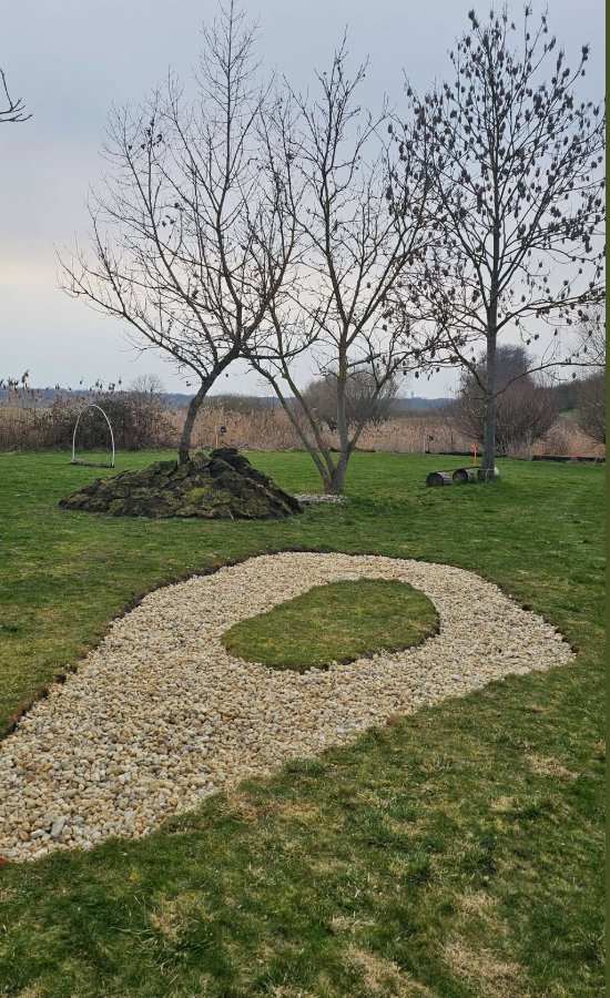 Pískový bankr (sand trap) ve tvaru kruhu na trávníku, v pozadí stoletá vrba